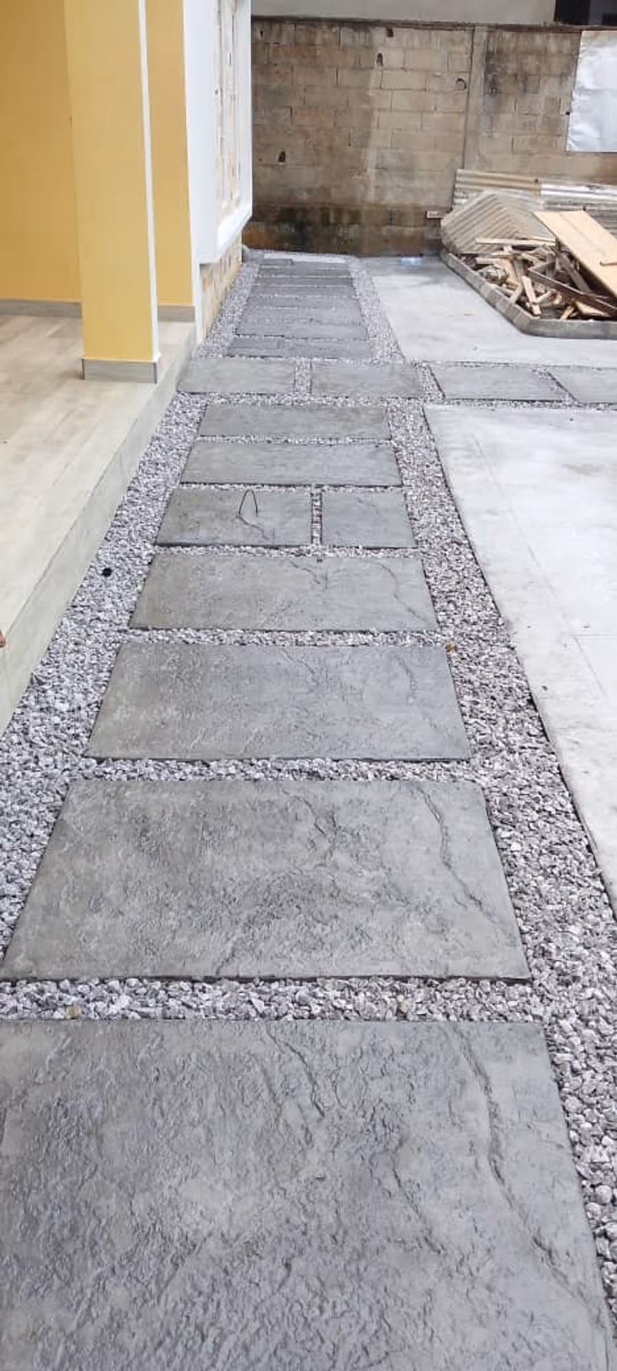 Pas japonais sur gravier. Dalles en béton imprimé posées à espacement régulier sur lit de gravier, entre deux bordures coulées.