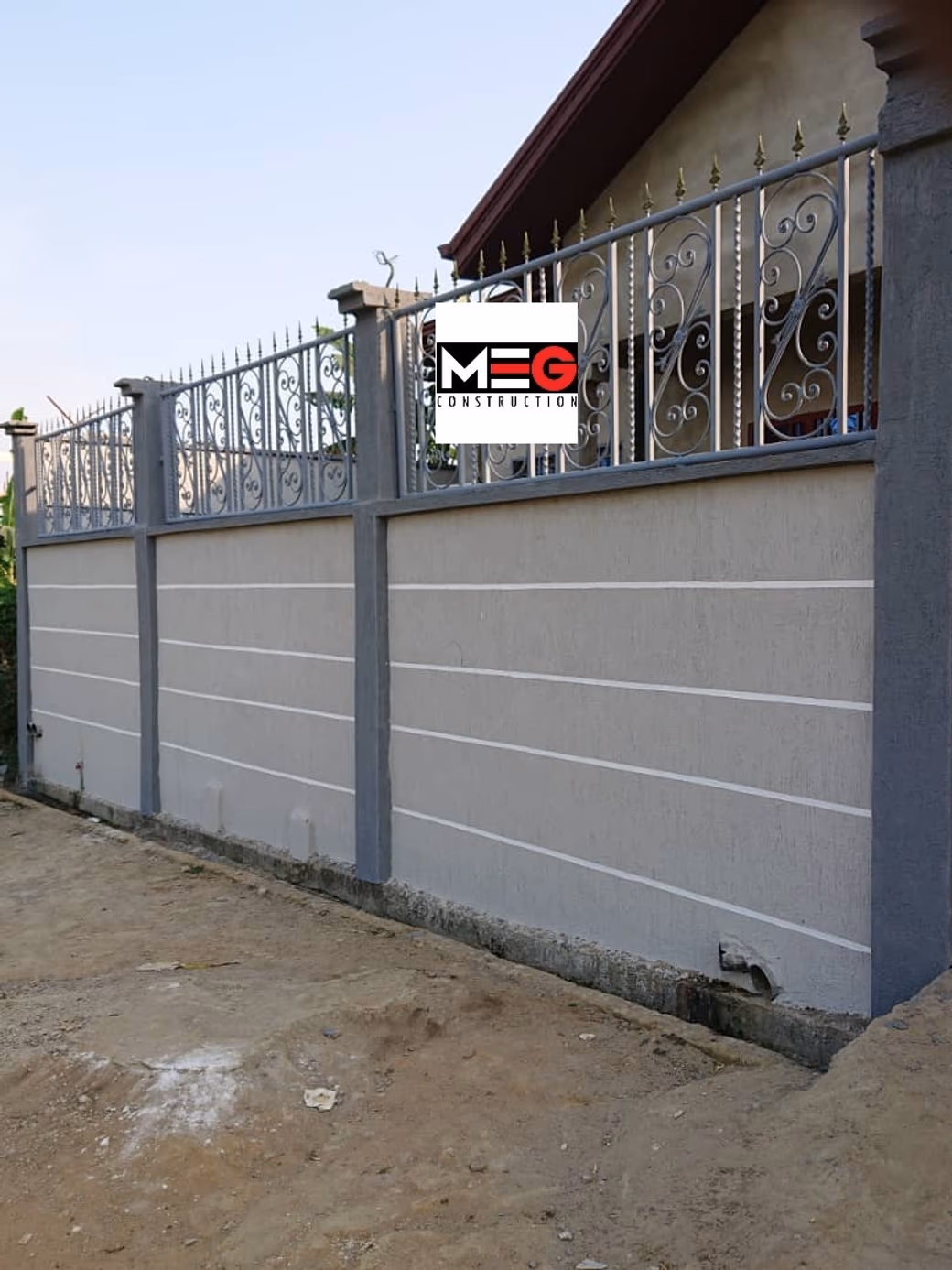 Mur de clôture en enduit gris refendu de joints creux horizontaux, dont chacun porte son ombre. Portail en fer forgé à l'arrière-plan