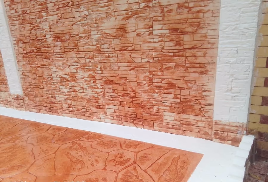 Parement en pierre éclatée. Mur habillé d’un parement teinte terre cuite à arêtes vives, plinthe claire, sol en béton imprimé assorti.